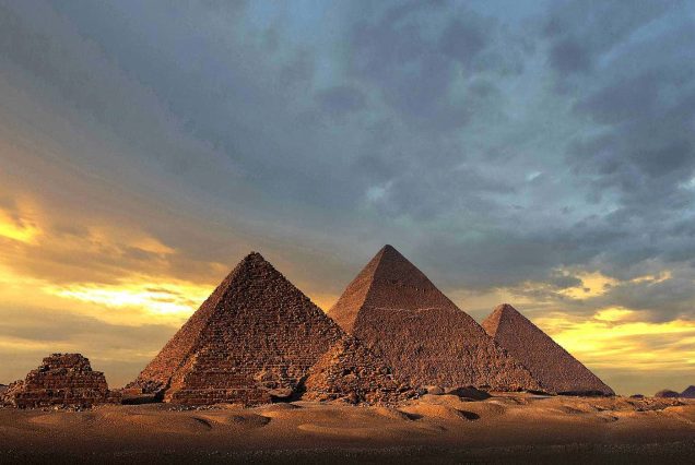 the pyramids of giza shadowed by an overcast sky